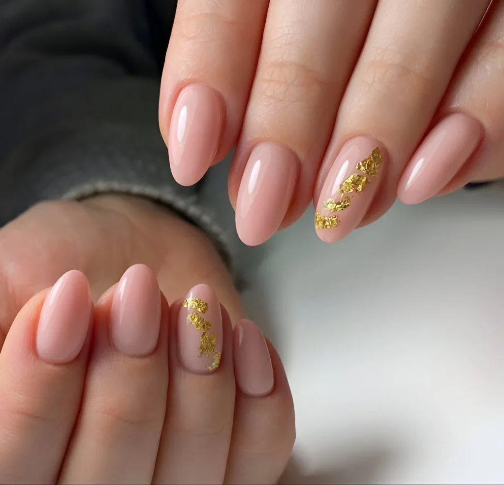 Blush-pink almond-shaped nails with gold flake accents.