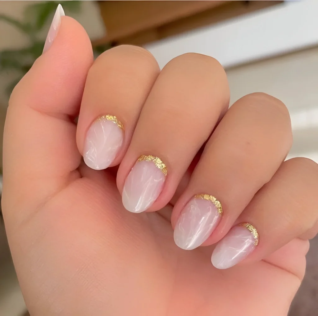 Oval-shaped nails with a milky white base and gold accents along the cuticle.