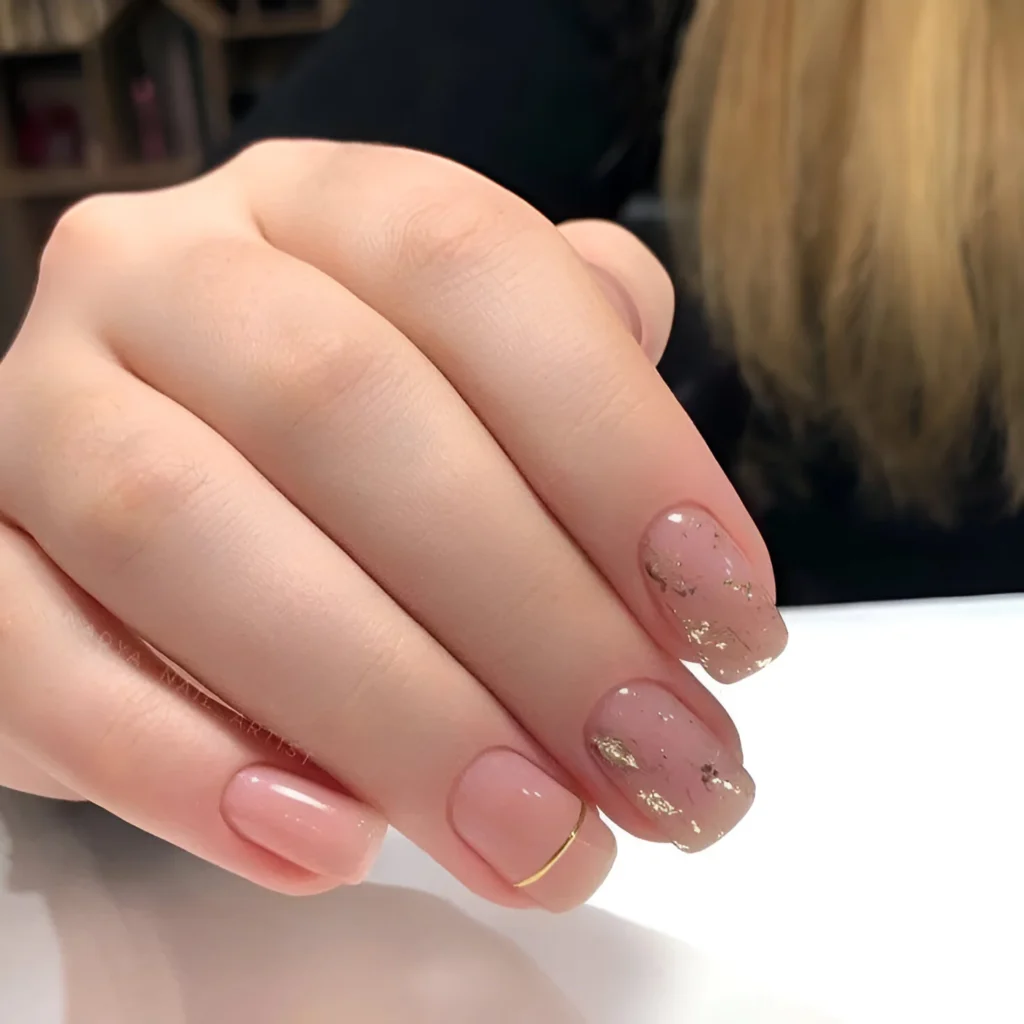 Short gelish nails with nude-pink polish and gold flake accents.