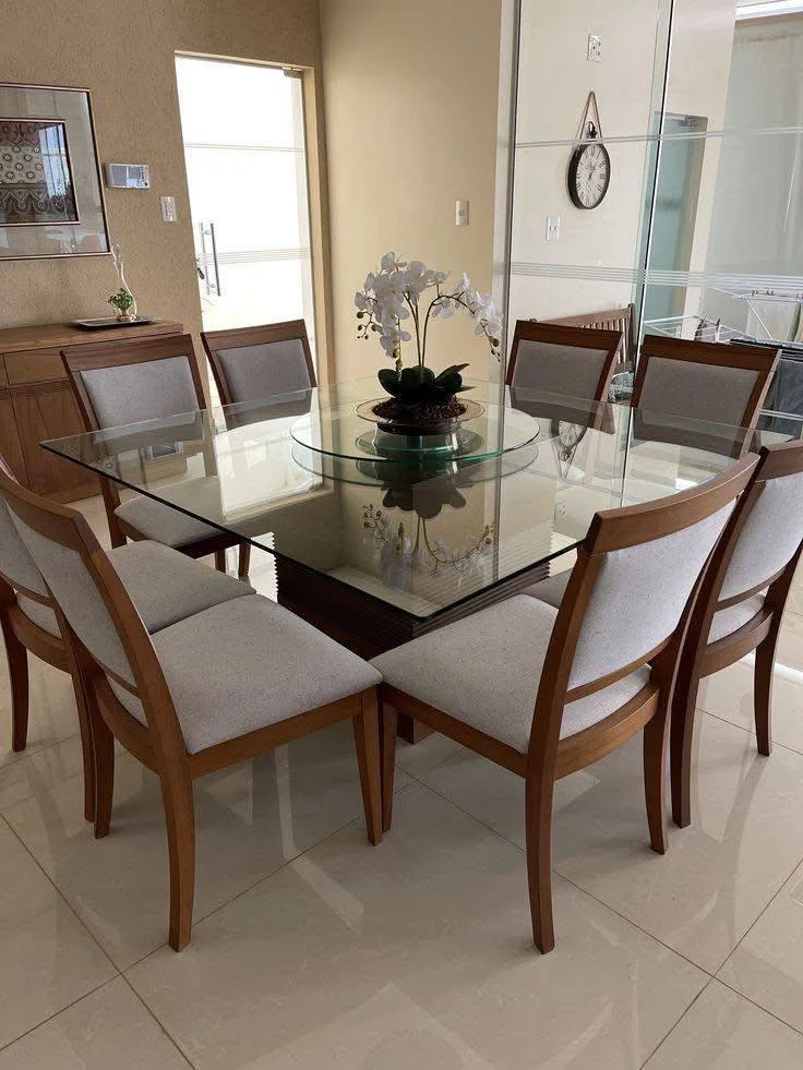 Dining room with a glass-top table, showcasing the wooden chair frames and neutral upholstery.