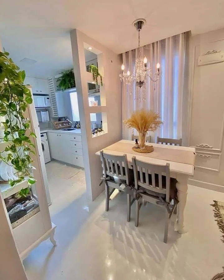 Dining nook defined by an architectural niche, featuring a light-colored table and a chandelier.