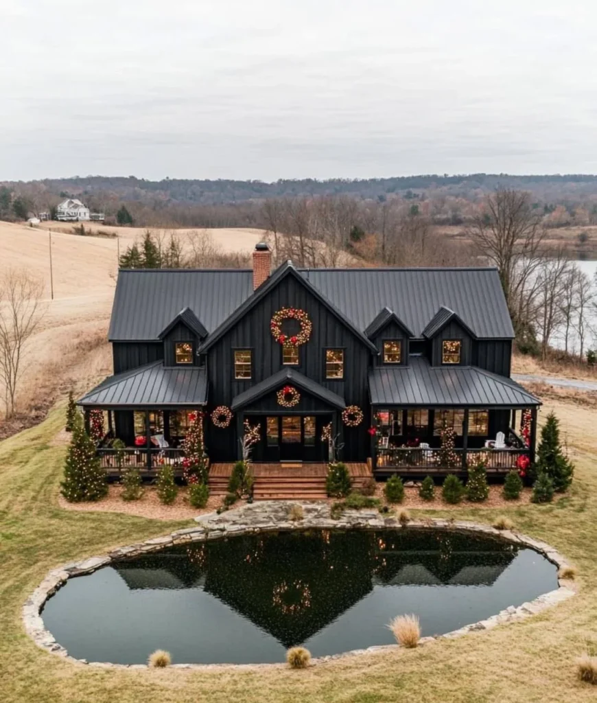 Black modern farmhouse with holiday decorations and a reflecting pond.