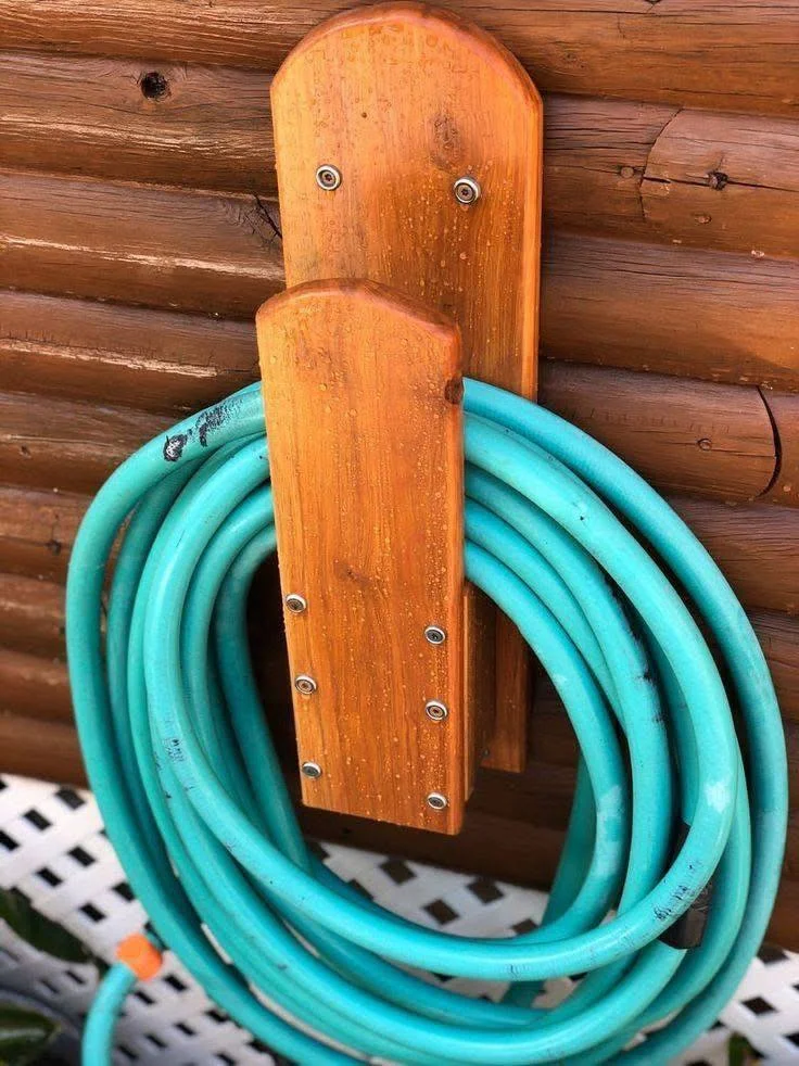 Wall-mounted wooden hanger holding a coiled garden hose, preventing tangles and keeping it off the ground.