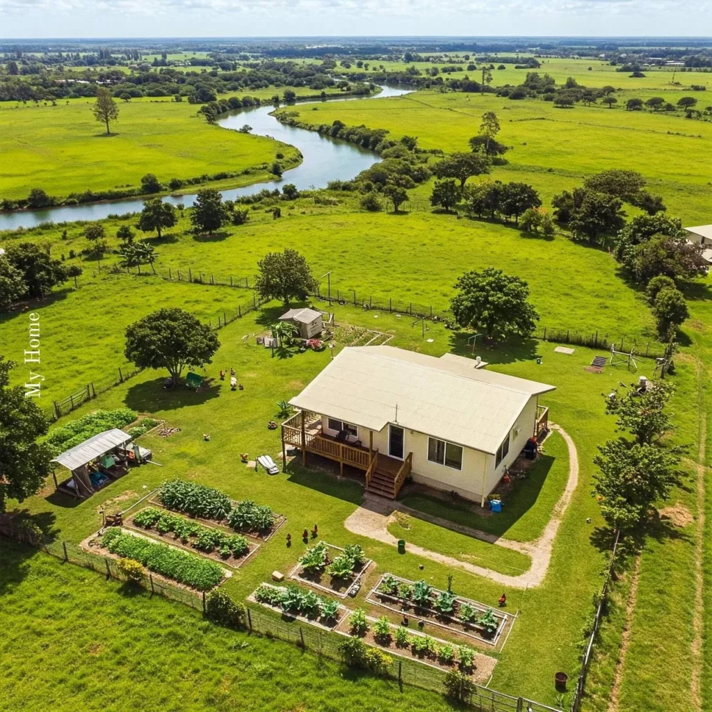 Rustic homestead with corrugated metal roof and abundant garden beds near a river.