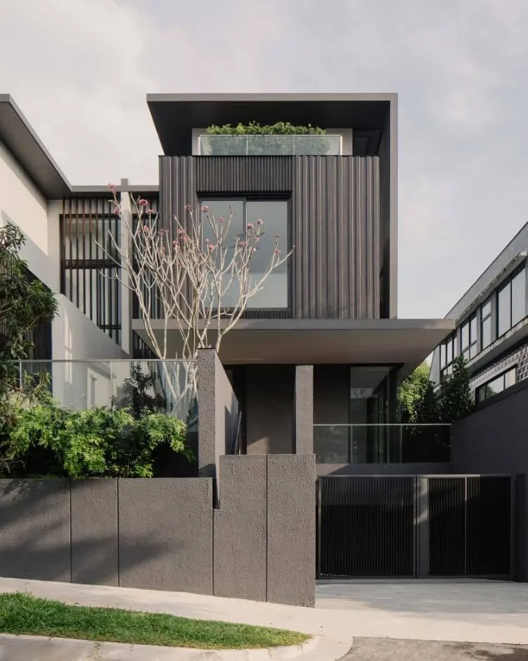 Modern industrial-style house design with dark facade, glass railings, and vertical greenery.