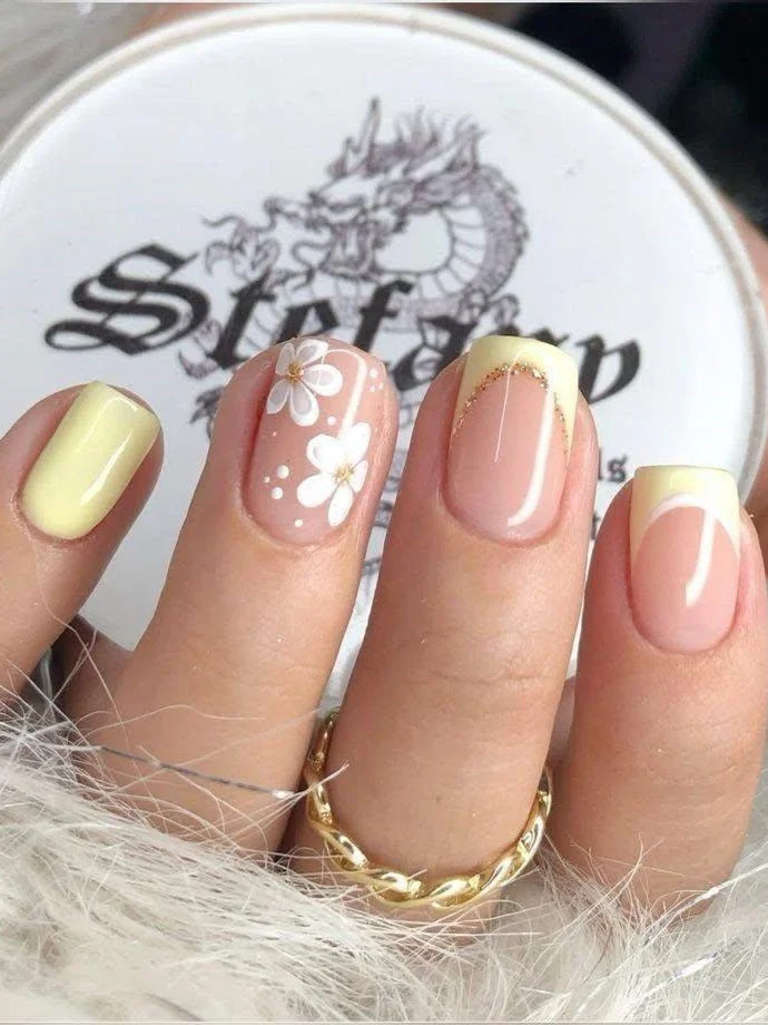 Short pink and yellow nails with mismatched designs, including daisies and French tips.