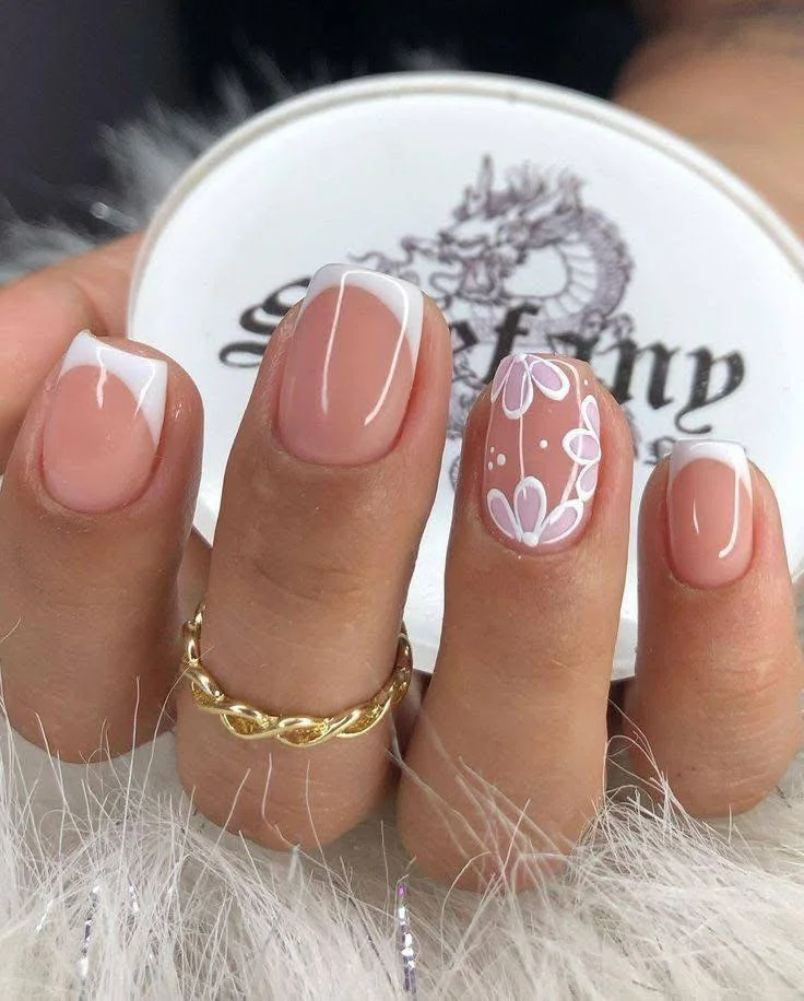 Short pink and white nails with a mix of French tip designs and floral patterns.