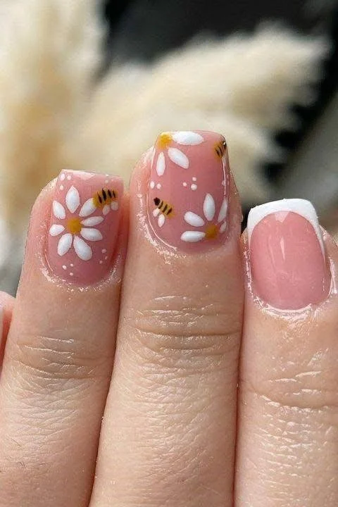 Short pink nails with daisy and bee nail art, and one French tip accent nail.