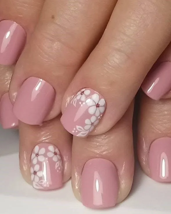 Short dusty rose nails with white flower nail art and rhinestone accents.