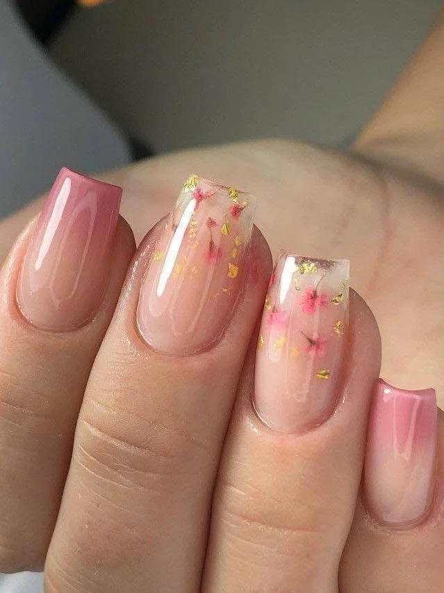 Short clear acrylic nails with encapsulated dried flowers and gold foil.