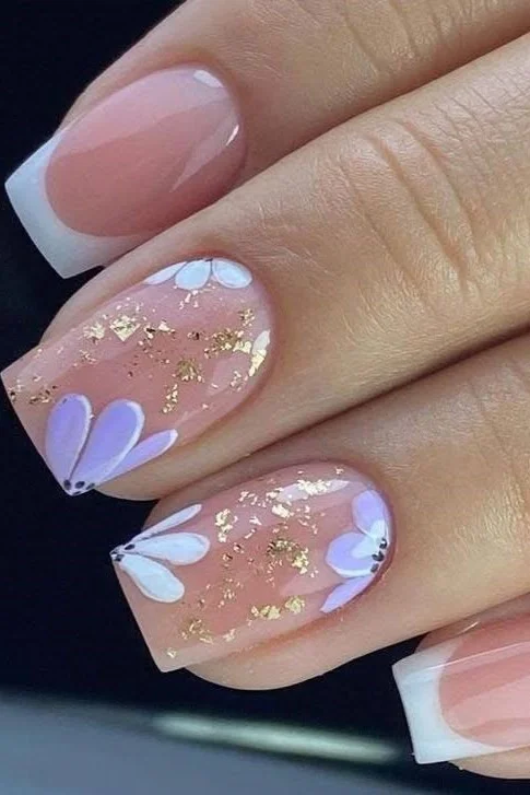 Short nails with lavender and white flower nail art, gold foil accents, and French tips.