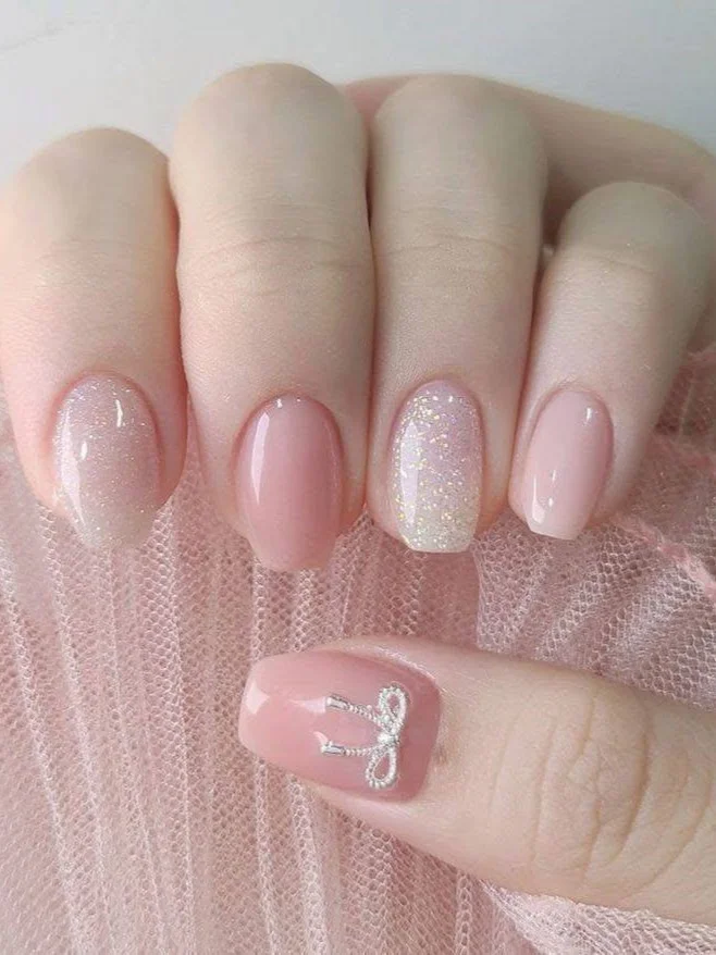 Short light pink nails with silver bow accents and glitter.