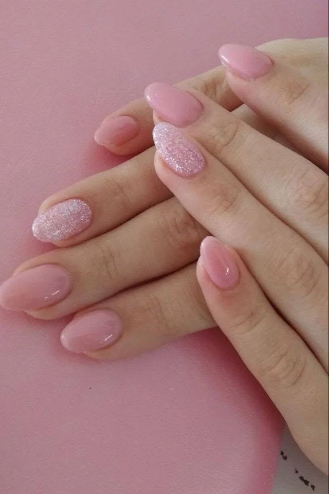 Short, light pink nails with two glitter accent nails.