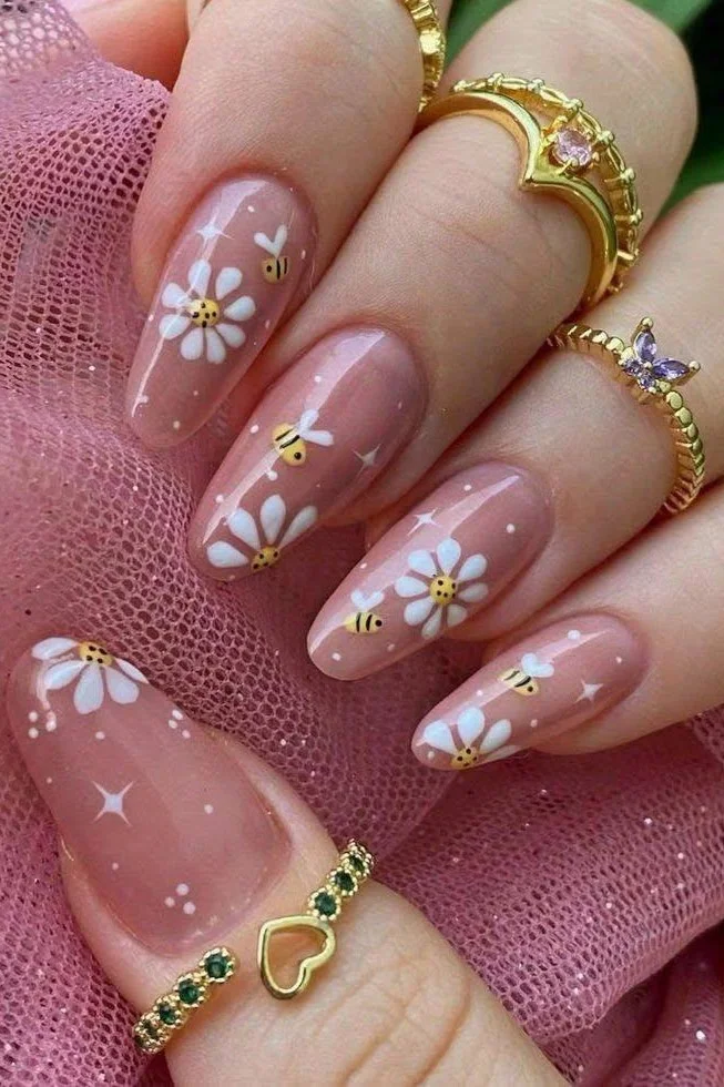 Short pink almond-shaped nails with bee and flower nail art.