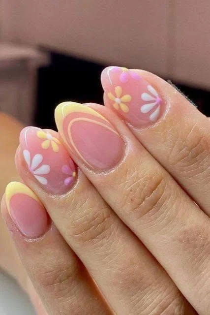 Short pastel pink and yellow nails with curved designs and small flower accents.