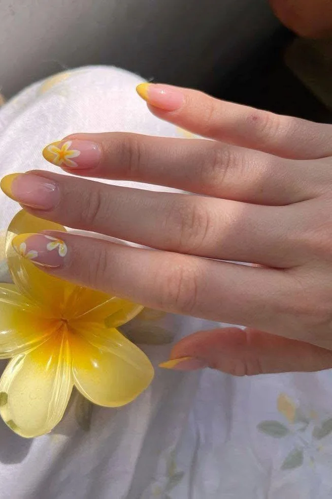 Short nails with yellow French tips and small white flower accents.