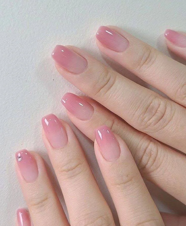 Short, light pink gradient nails with small rhinestone detail.