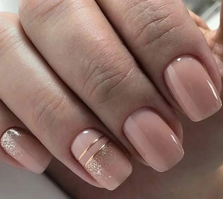 Short, peachy-pink nude nails with rose gold stripe and glitter accents.