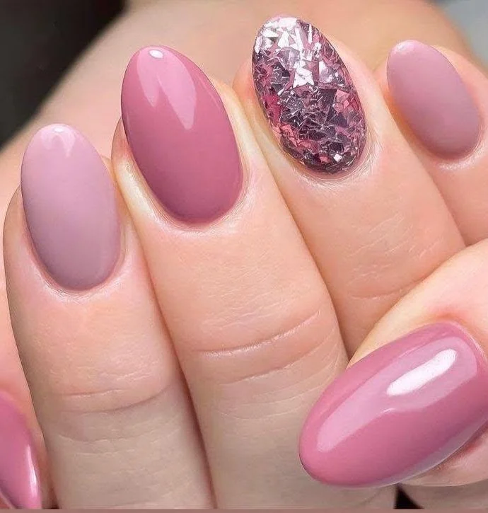 Short nails with different shades of pink and mauve, and a glitter accent.