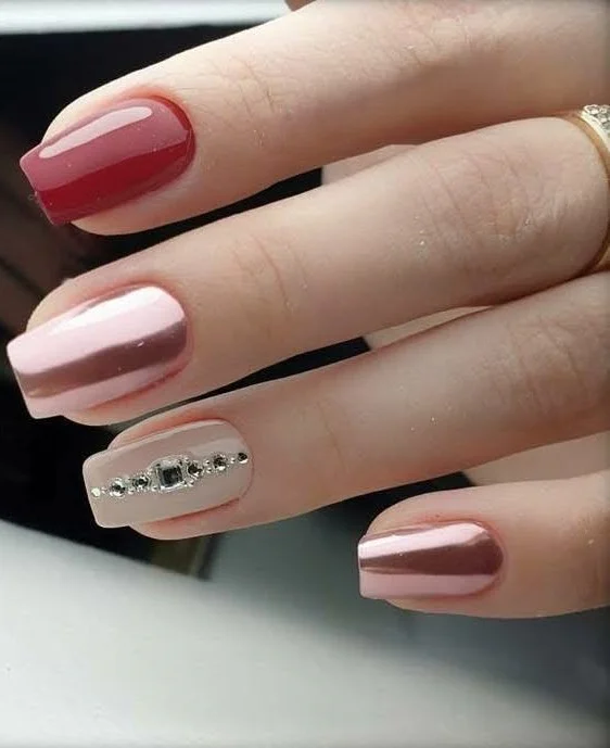 Short nails with deep rose, rose-gold chrome, and rhinestone accents.