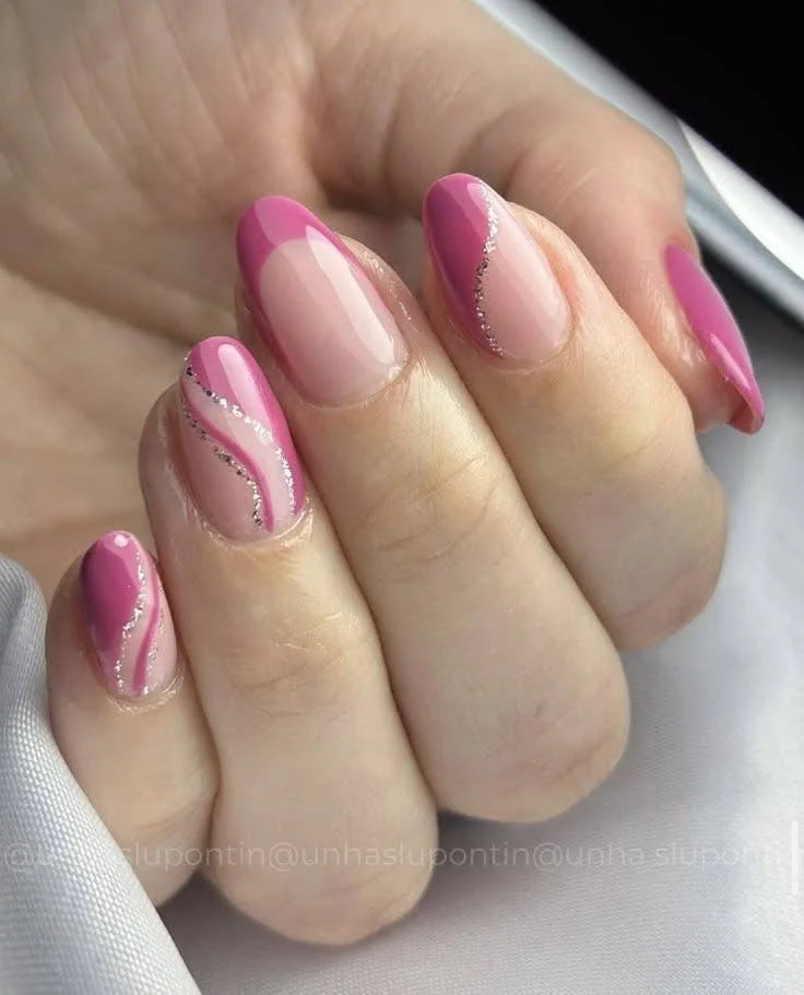 Short nails with abstract pale and bright pink designs, silver glitter accents.