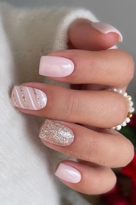 Short, pale pink nails with diagonal white and glitter stripes.