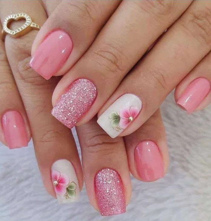 Short pink nails with pink glitter and floral accent nails.