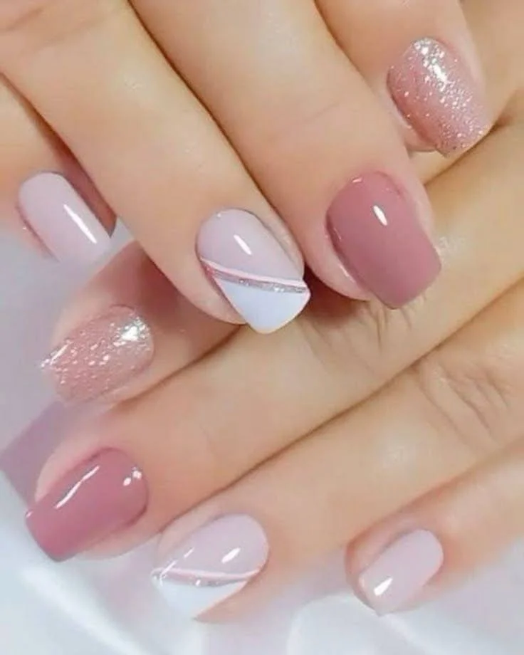 Short mauve nude nails with white and glitter swirl accents.