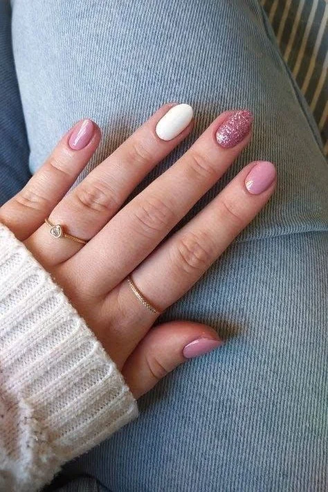 Short almond nails with pink nude, white, and glitter accents.