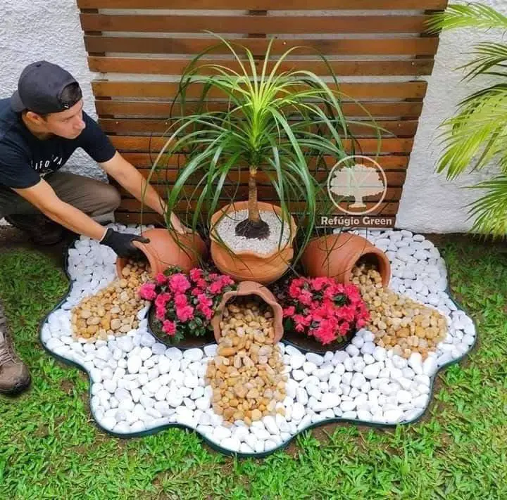 Garden feature with a ponytail palm and flowers, surrounded by a decorative arrangement of white and tan river stones.