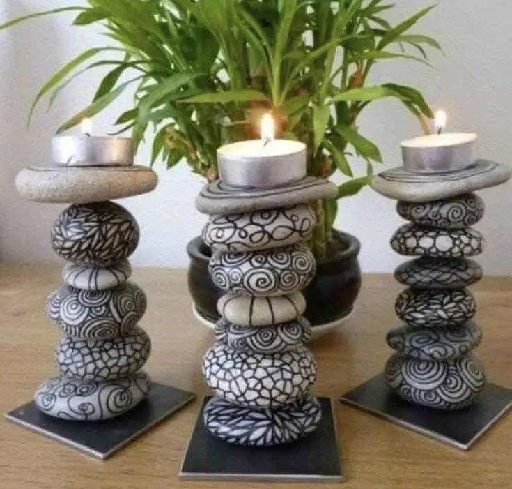 Three stacked river stone candle holders with intricate black and white painted designs, holding lit tea light candles.