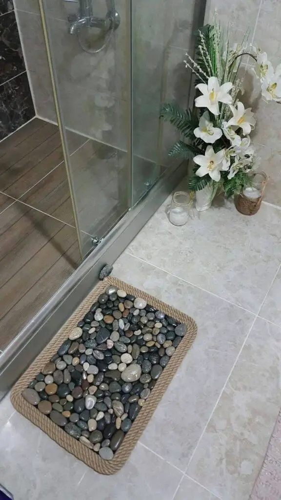 Rectangular area of river stones within a tiled bathroom floor, framed with a rope border, near a shower.