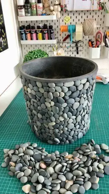 DIY project showing a plain planter being covered with small, grey river stones.