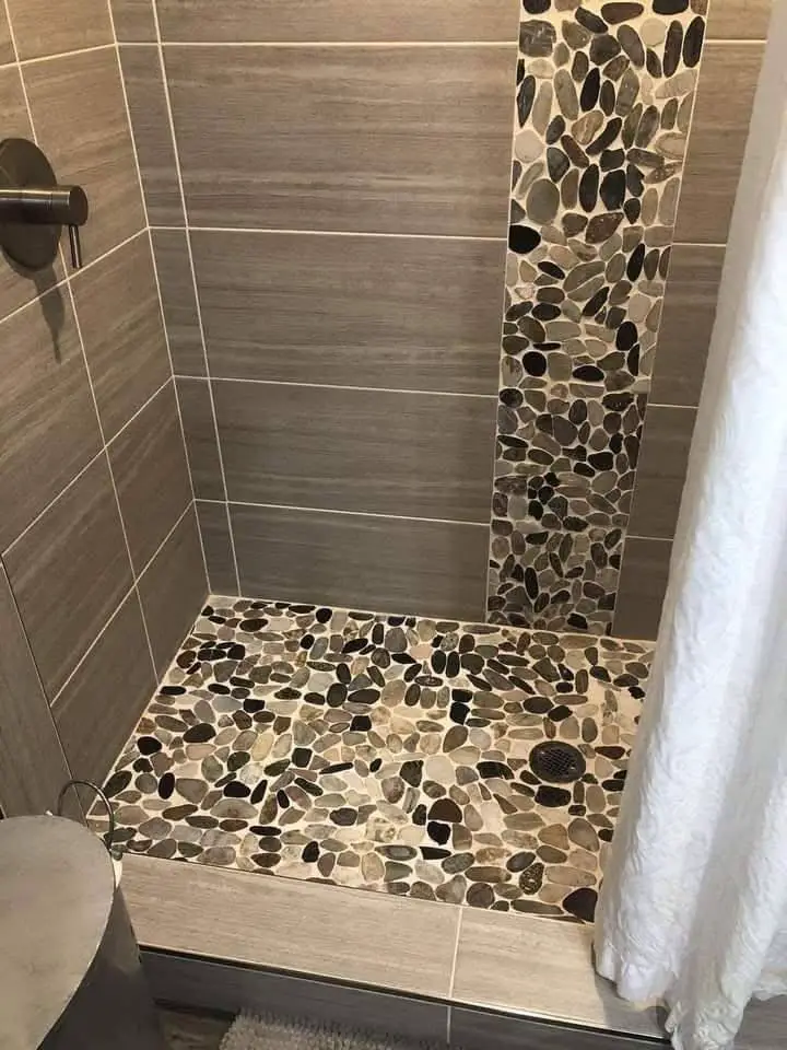 Shower with a vertical strip of river stone tile on the wall and a larger section of river stone tile on the floor.