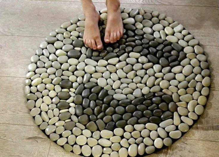 Round DIY pebble carpet made of smooth, various-colored river stones, with bare feet stepping on it.