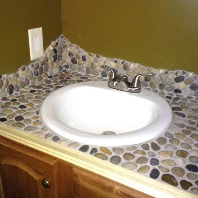 Bathroom countertop featuring a mosaic of small, multi-colored river stones surrounding a white sink.