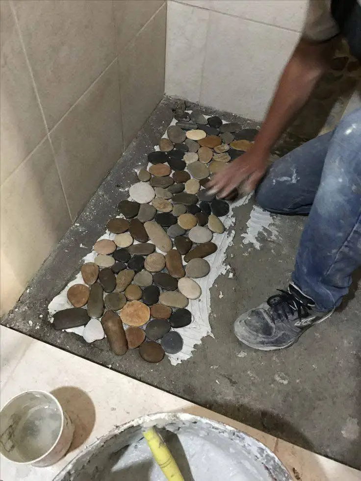 Person installing a river stone floor in a shower, applying stones to a mortar base.