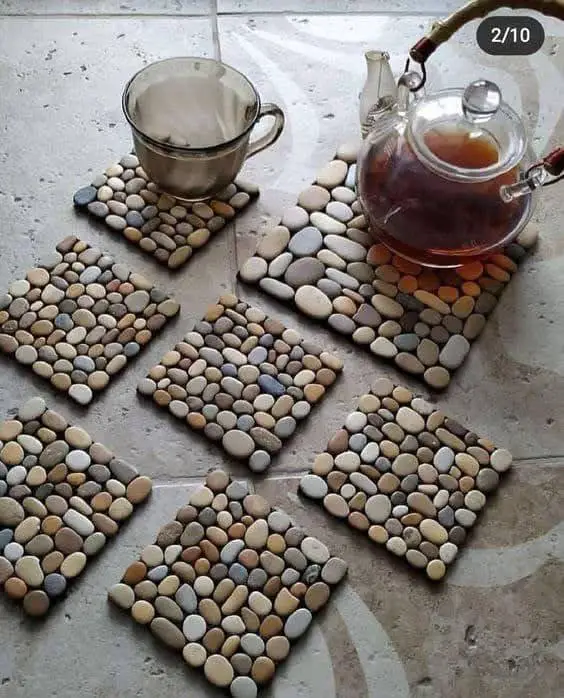 Set of square DIY coasters made from small, multi-colored river stones, with a teacup and teapot resting on them.