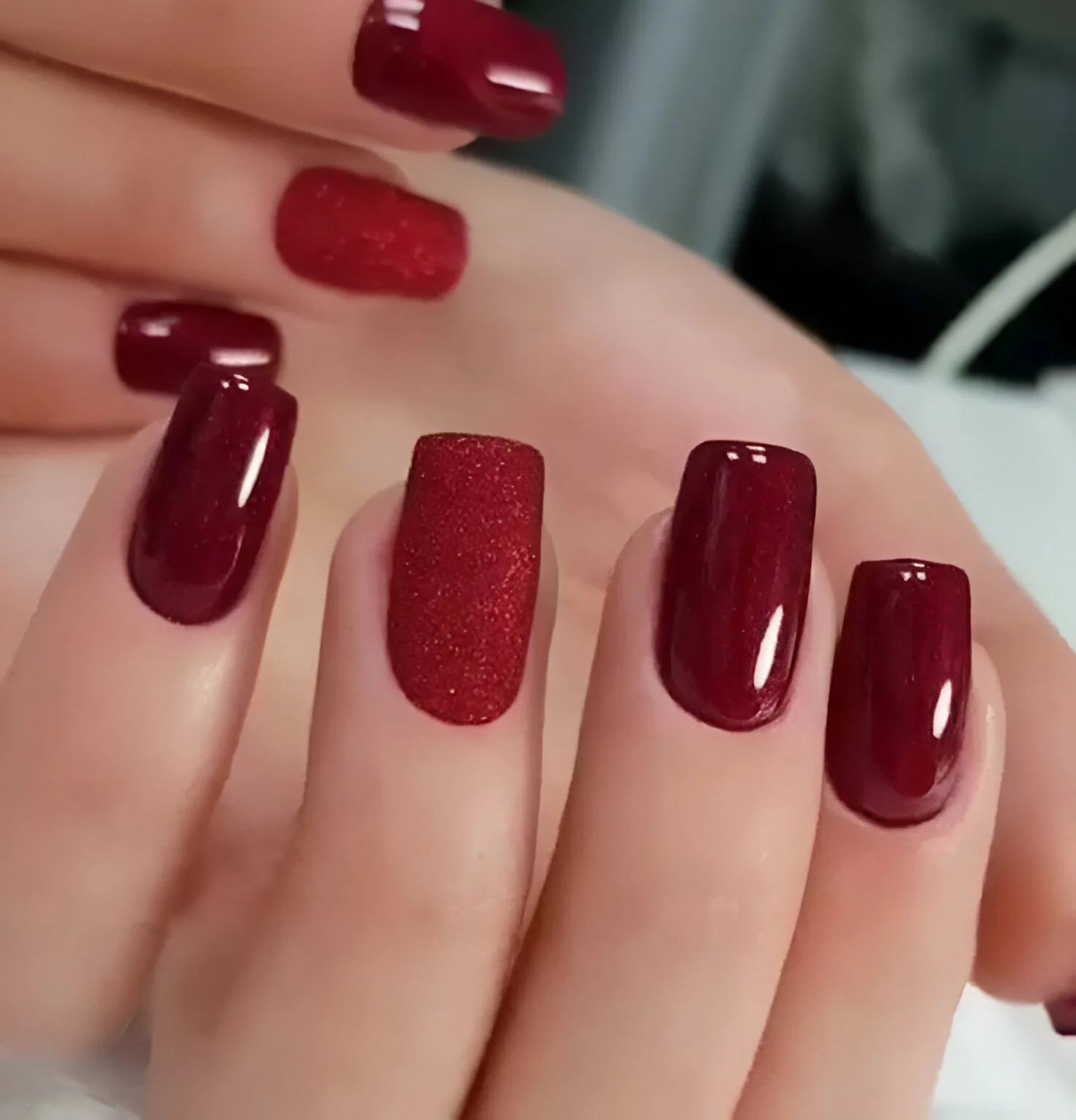 Dark red nails with textured glitter accent.