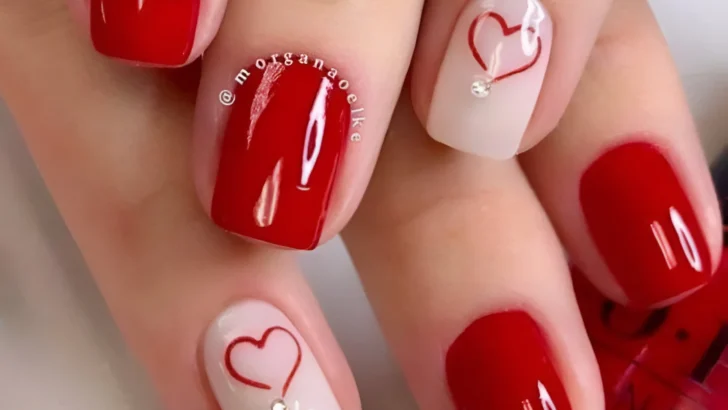 Minimalist red nails with small white heart accents, a sweet 2025 design.