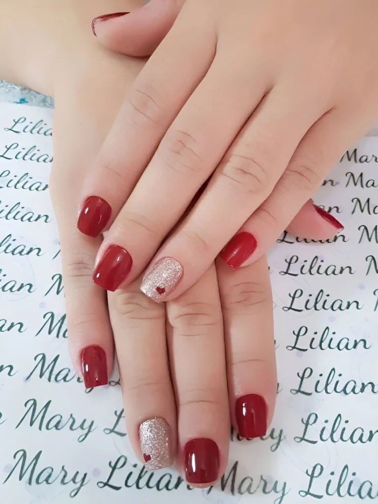 Classic red nails with a glitter accent nail and a delicate heart detail for 2025.