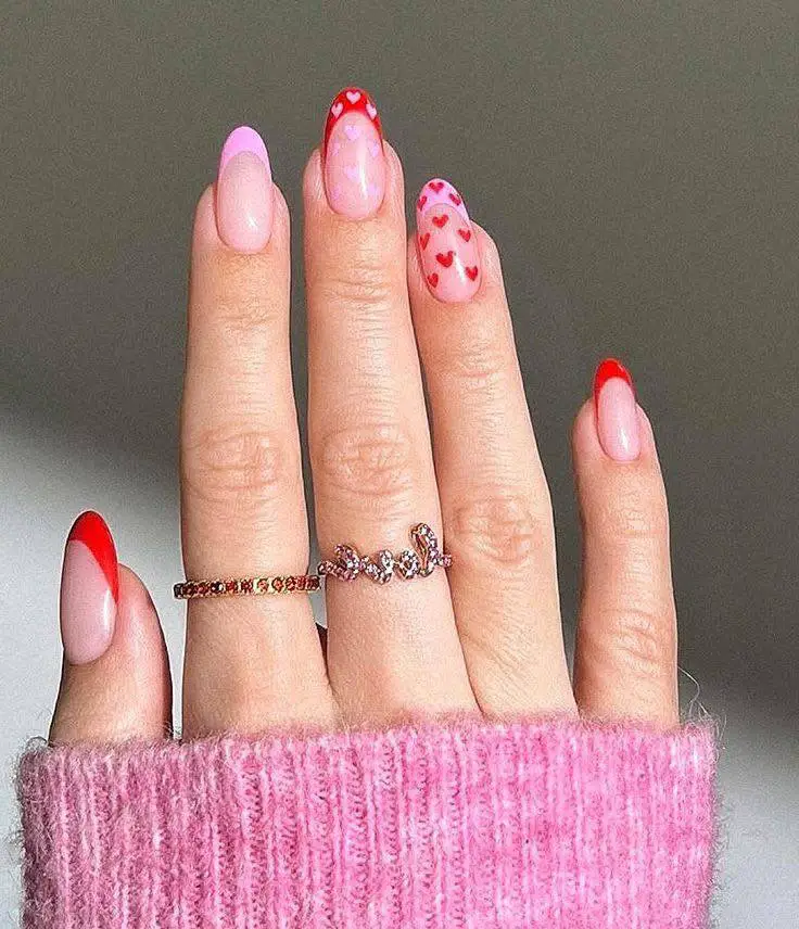 Almond nails with red and pink French tips and one nail with tiny red hearts.