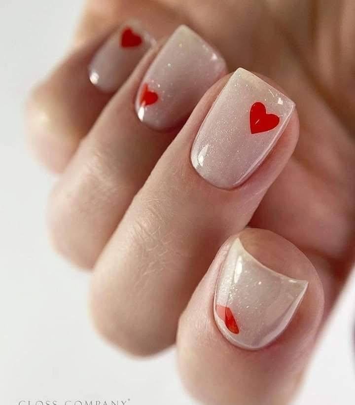 Short square nails with sheer, shimmery pink polish and a single red heart on each nail.