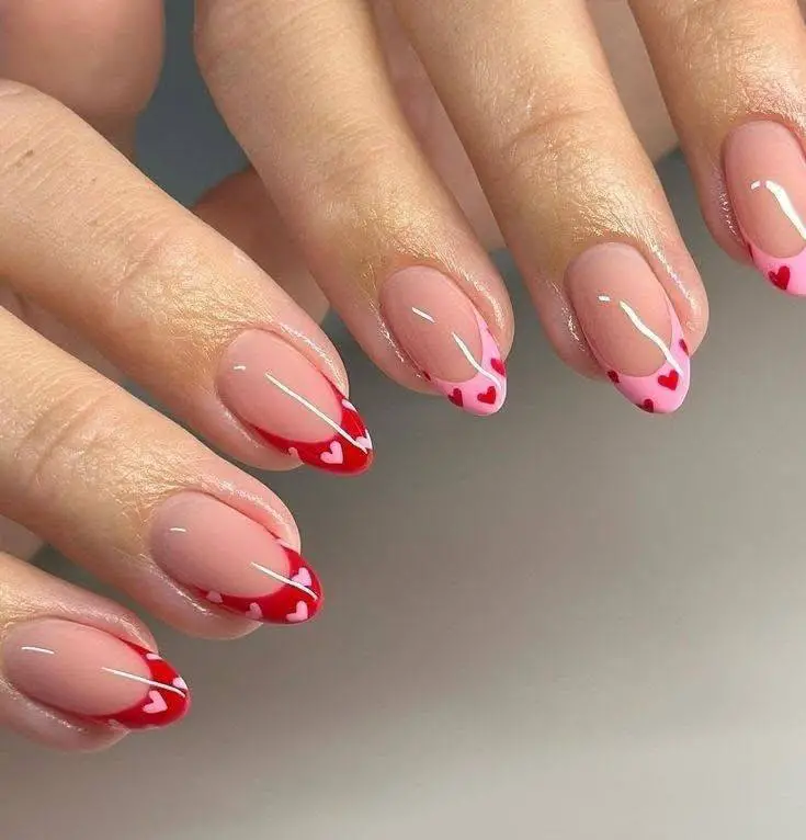 Oval nails with a sheer base and French tips made of tiny red and pink hearts.