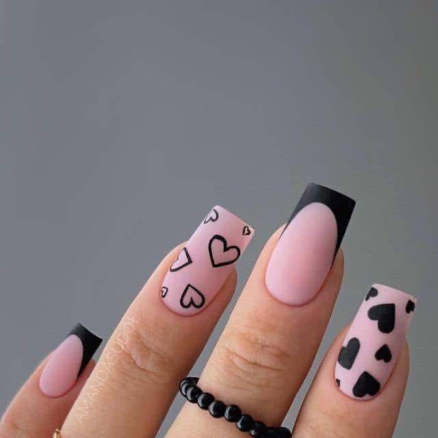 Long coffin nails with matte pink polish, black outlined hearts, and black heart accents.