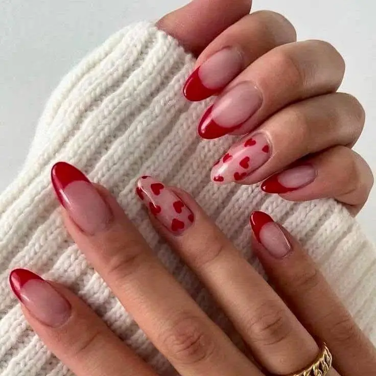 Almond-shaped nails with sheer pink base, red French tips, and small red heart details.