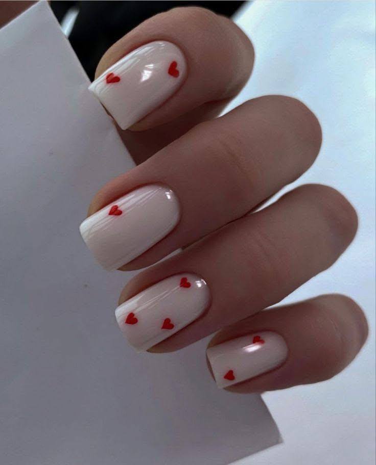 Square nails with creamy off-white polish and small red heart accents.