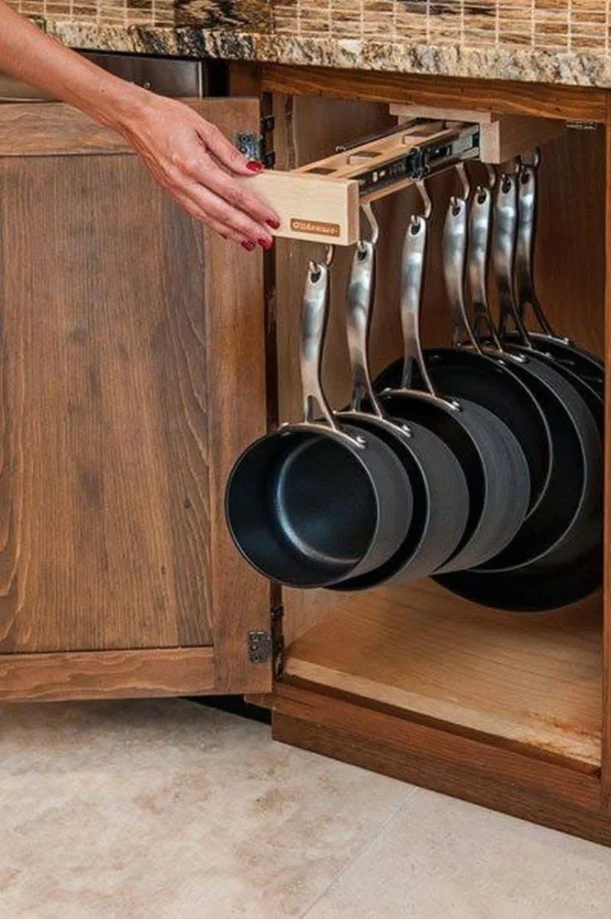 Pull-out rack with hanging pots and pans inside a kitchen cabinet.