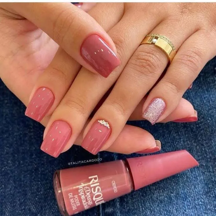 Short, vibrant red nails with a silver glitter accent nail featuring a small heart detail, displaying a glamorous and chic look.