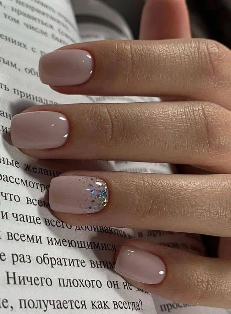 Short nude nails with a single glitter accent nail, demonstrating a glamorous and subtle design.